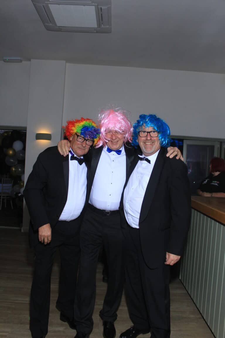 Three men in tuxedos wearing colourful wigs